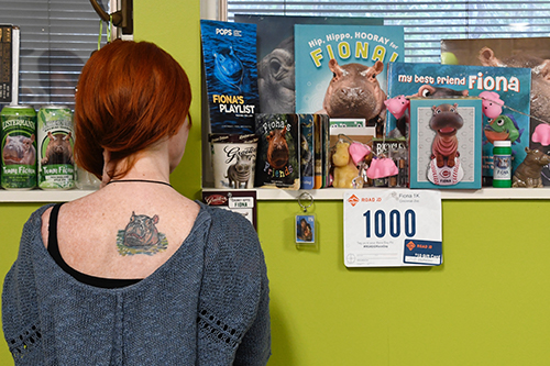 Michelle shows her Fiona tattoo on her upper back with her office window in the background, decorating with Fiona merchandise.